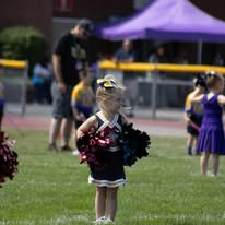 Young Titans cheerleader standing on the field with pom-poms