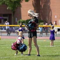 Young cheerleader with pom-poms alongside a coach on the field