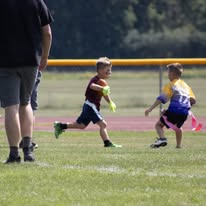 Young flag football player running with a defender chasing