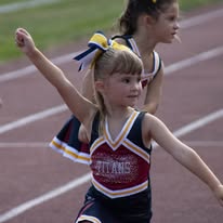 Little Titans cheerleader with pom-poms raised on the track